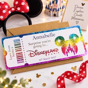 May include: A rectangular Disneyland Paris gift ticket featuring a rainbow glitter border and a Mickey Mouse head silhouette with a castle graphic. The text reads Annabelle, Surprise you're going to, Disneyland Paris, 16th March 2027, and Love from Santa x.