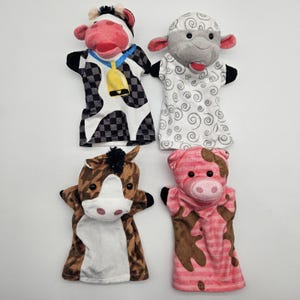 May include: Four plush animal hand puppets: a cow, a sheep, a horse, and a pig. The cow puppet is black and white with a bell. The sheep is gray and white with a curly pattern. The horse is brown and white. The pig is pink with brown spots.