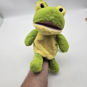 May include: A plush frog puppet with a green head and limbs, and a yellow body. The frog has large black eyes and a wide open mouth. The puppet is designed to be worn on the hand.