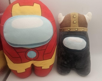 May include: Two plush toys shaped like the characters from the game Among Us. One is red and yellow and has a design resembling Iron Man. The other is black and has a Viking helmet.