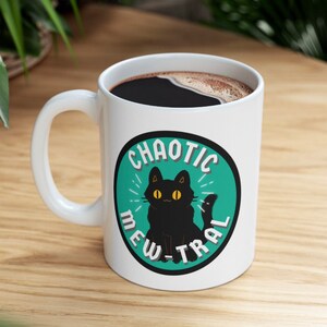 May include: White ceramic coffee mug with a black cat illustration and the text "Chaotic Mew-tral" in a teal circle.