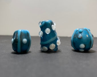 Trio of dark turquoise, opaque glass beads in funky shapes, decorated with raised and opaque light turquoise stripes