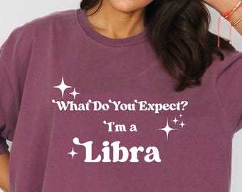 May include: Berry-colored t-shirt with the text "What Do You Expect? I'm a Libra" in white. The shirt has a relaxed fit and short sleeves. A color swatch in the upper left corner reads "Berry".