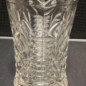 May include: A clear glass pitcher with a diamond pattern. The pitcher has a wide mouth and a handle.
