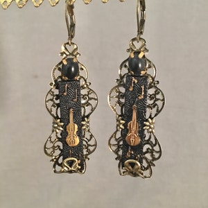 May include: A pair of gold filigree earrings with black and gold musical note and violin designs. The earrings have black beads at the top.