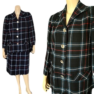May include: A vintage two-piece suit featuring a black, blue, red, and white plaid pattern. The suit includes a collared jacket with button closures and a matching skirt. The jacket has pockets and the suit is displayed on a mannequin.