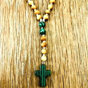 May include: A rosary with wooden beads and green malachite accents. The cross pendant is made of green malachite. The beads are strung on a white cord, creating a religious accessory.