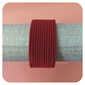 Op de afbeelding: Een stapel rode fluwelen armbanden. De armbanden zijn in een cirkel gerangschikt en zijn gemaakt van een zacht, pluche materiaal.