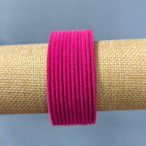 May include: A stack of pink velvet bangles. The bangles are arranged in a circle and are on a brown burlap background.