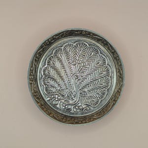 Op de afbeelding: Een zilveren metalen dienblad met een ingewikkeld ontwerp van een pauw met zijn uitgespreide staartveren.