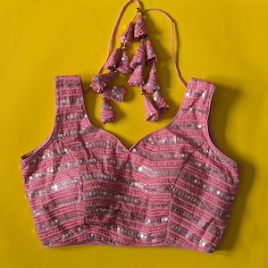 Puede incluir: Blusa rosa sin mangas con lentejuelas y un detalle de borla decorativo.