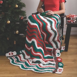 May include: A woman sits on a chair with a crocheted blanket in red, white, and green. The blanket has a wavy pattern and a scalloped edge.