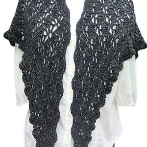 Puede incluir: Un chal de ganchillo negro con un delicado patrón de calado. El chal está drapeado sobre una camisa blanca.