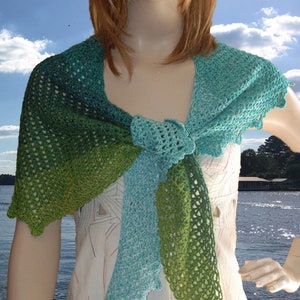 May include: A green and blue crocheted shawl with a scalloped edge. The shawl is tied in a knot at the neck.