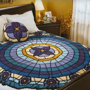 May include: A handmade, round crochet blanket in shades of blue, purple, and yellow, resembling a stained-glass window. A matching pillow is on the bed. The blanket is approximately 70 inches in diameter, perfect for a bedspread.