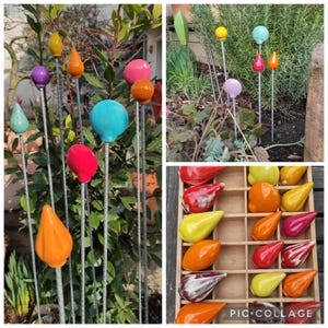 Könnte beinhalten: Bunte Gartenstecker mit verschiedenen Formen, darunter Kugeln, Tropfen und Blätter. Die Stecker sind aus Metall und mit glänzenden Keramikteilen in Rot, Orange, Gelb, Blau und Lila verziert. Einige werden in einer Gartenumgebung präsentiert.