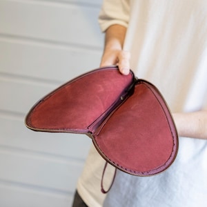 May include: A burgundy leather clutch purse with a zipper closure and a small handle. The purse is open and the inside is lined with a burgundy fabric.