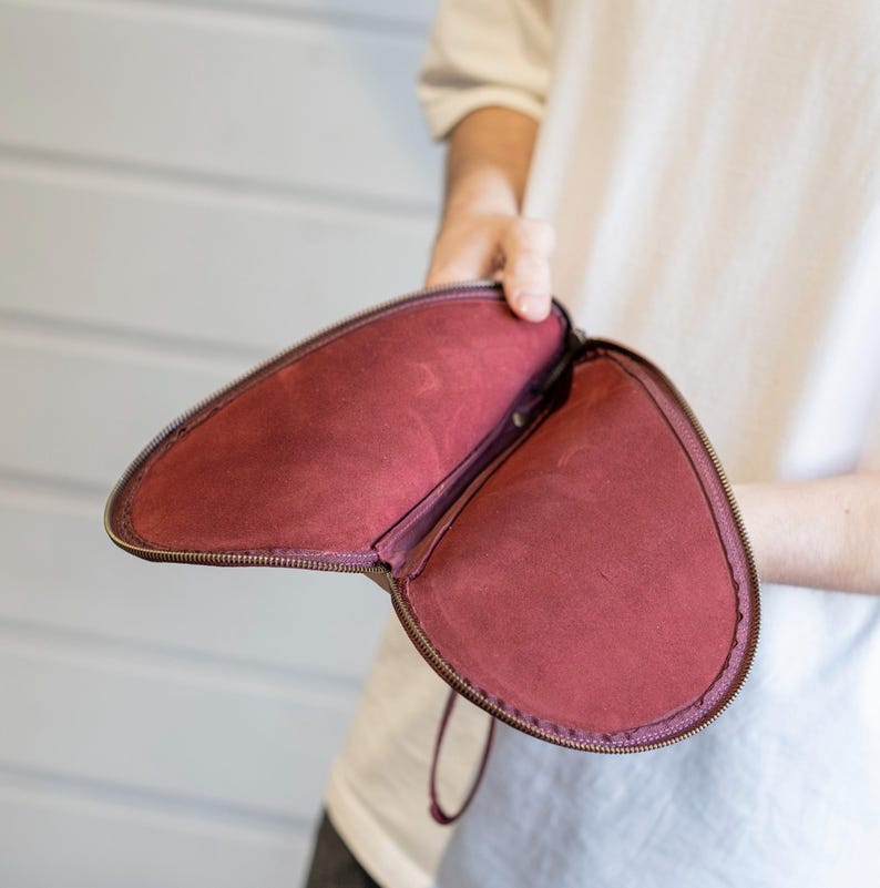 May include: A burgundy leather clutch purse with a zipper closure and a small handle. The purse is open and the inside is lined with a burgundy fabric.
