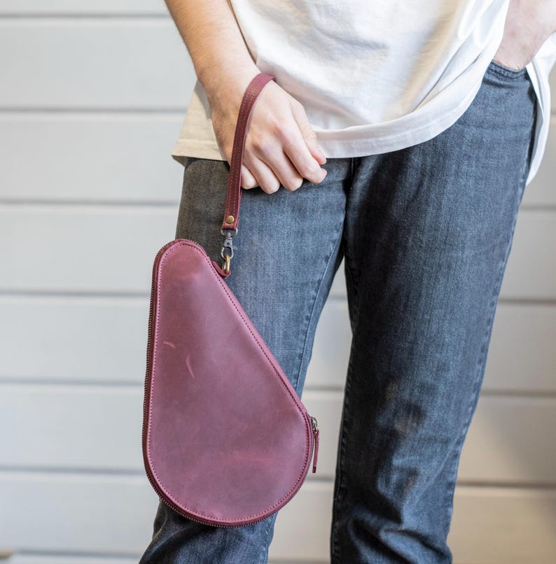 May include: A burgundy leather purse with a zipper closure and a long strap. The purse is shaped like a teardrop.