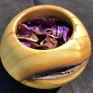 May include: A wooden bowl with a natural wood finish and a dark brown burn mark. The bowl is filled with dried purple and brown flower petals.