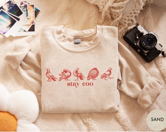 May include: A beige sweatshirt with a red graphic of five birds and the text "stay eco" printed on the front.