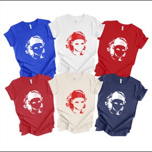 May include: Five t-shirts in different colors, each featuring a white silhouette of a person wearing a baseball cap with the number "28" on it. The t-shirts are blue, white, red, beige, and navy blue.