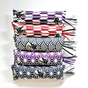 May include: Stack of six catnip pillows with various geometric patterns in purple, red, black, and blue. Each pillow features a black cat illustration and is adorned with colorful ribbons. The pillows are designed for cats.