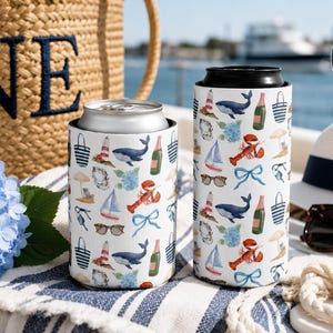 Könnte beinhalten: Zwei weiße Dosenkühler mit einem wiederkehrenden nautischen Muster aus Walen, Hummern, Segelbooten, Leuchttürmen, Champagnerflaschen, Sonnenbrillen und blauen Schleifen. Ein kreisförmiges Abzeichen oben rechts zeigt den Text SLIM & REGULAR CAN.