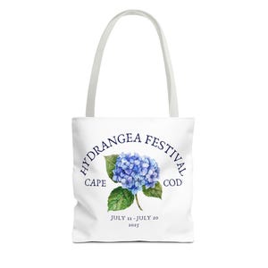 Op de afbeelding: Witte tote bag met een blauwe hortensia bloem grafische en de tekst "Hydrangea Festival Cape Cod July 11 - July 20 2023"