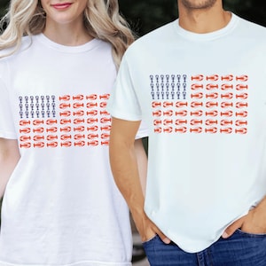 May include: White t-shirts with a flag design made of red lobsters and blue lobster trap graphics. The shirts are short-sleeved and worn by two people. The design is a patriotic theme.