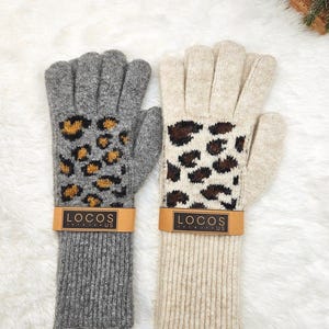 以下が含まれることがあります： 2組のニット手袋。片方は茶色と金色のヒョウ柄のグレー。もう片方は茶色のヒョウ柄のベージュ。各ペアには「LOCOS US」の文字が入った茶色の紙バンドが付いています。