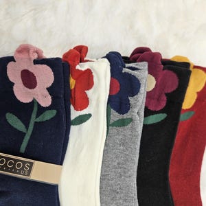 May include: A collection of colorful socks featuring a flower design. The socks come in navy, white, gray, black, and red, each with a different colored flower. The brand name "LOCOS" is visible on a brown label.