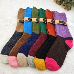 May include: A selection of colourful wool socks, each with a unique colour combination. The socks are arranged side by side, showcasing a variety of hues including blue, green, orange, and purple. Each pair is banded with a brown label that reads "LOCOS".