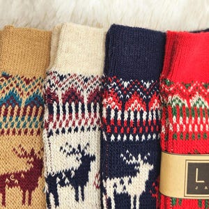 Puede incluir: Una colección de calcetines de punto coloridos con renos y patrones geométricos. Los calcetines son en tonos azul marino, beige, crema, rojo y azul. Los calcetines tienen un puño acanalado y un diseño estampado. La marca "LOCOS" es visible en una etiqueta marrón.