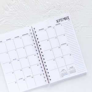 May include: A white monthly calendar with a black spiral binding. The calendar is open to September 2024. The days of the week are labelled at the top of the calendar. The calendar has a small calendar for August and October on the right side.