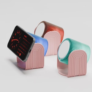 Può includere: Uno smartphone con un calendario digitale rosso è appoggiato su un supporto rosa, accanto a tre stazioni di ricarica colorate e a coste in blu, rosso-marrone e verde acqua. Le stazioni hanno cime circolari bianche.