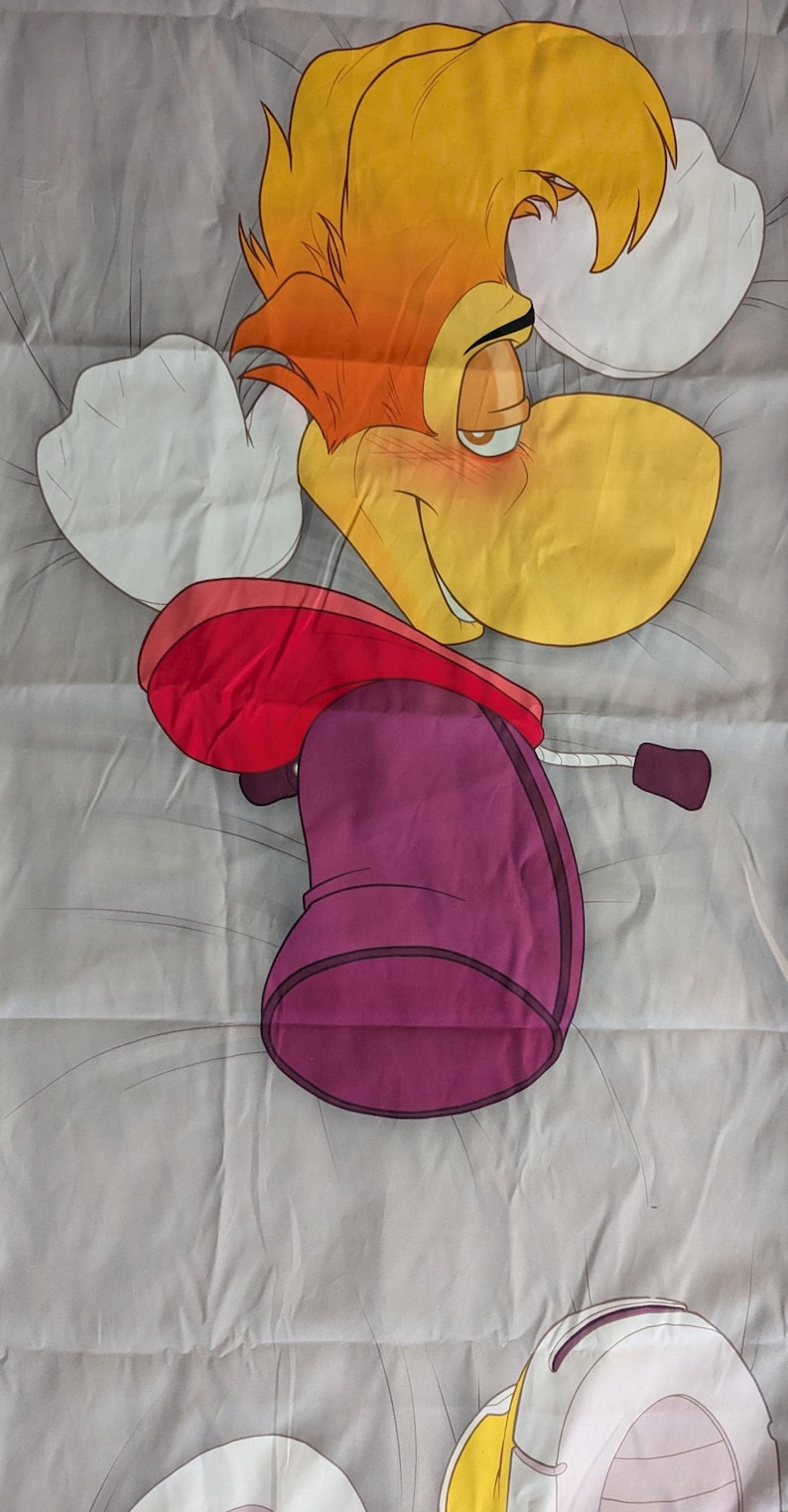 May include: A cartoon character pillowcase featuring a yellow-faced character with orange hair, a red hat, and a purple body. The character is lying on a gray background with white accents. The design is a vibrant and playful.