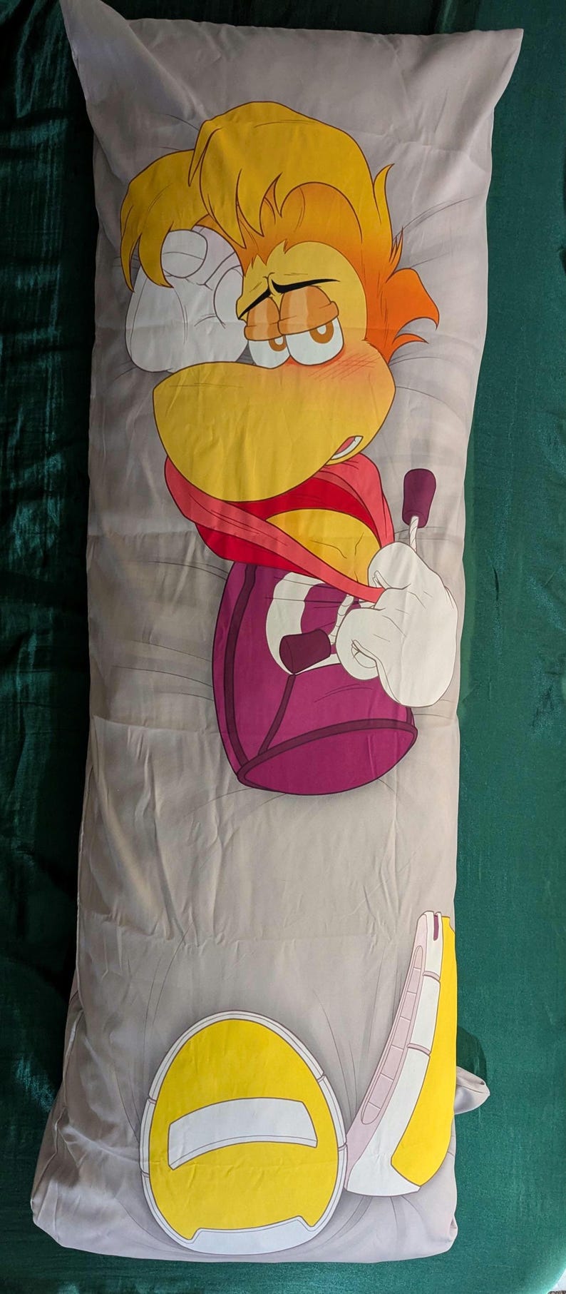 May include: A long, gray body pillow featuring a cartoon character with yellow hair, a yellow beak, and a red scarf. The character's body is purple, and the pillow has a yellow and white design at the bottom.
