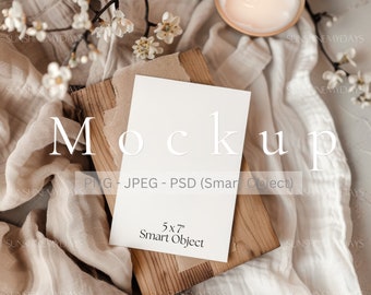 May include: A white 5x7 inch card mockup on a wooden surface with a beige fabric background. The card is a smart object and can be customized with your own design.