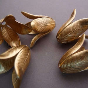 May include: Four gold-colored metal flower-shaped embellishments with a textured surface. The embellishments are arranged in a cluster on a gray background.