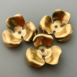 以下が含まれることがあります： 5枚の花びらを持つ金色の金属製のフラワーシェイプが3つ。花びらはわずかに湾曲しており、表面にテクスチャがあります。