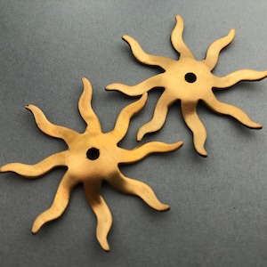 May include: Two gold-colored metal sunburst shapes with eight points each. The sunbursts have a hole in the center.