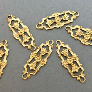 Könnte beinhalten: Sechs goldfarbene, dekorative Metallverzierungen mit filigranen Blumenmustern. Jede Verzierung hat oben und unten zwei Schlaufen zum Anbringen an anderen Gegenständen.