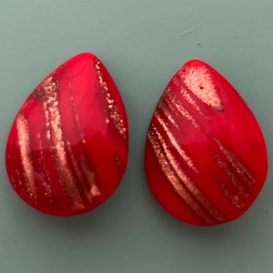 May include: A pair of red teardrop-shaped earrings with gold glitter accents.