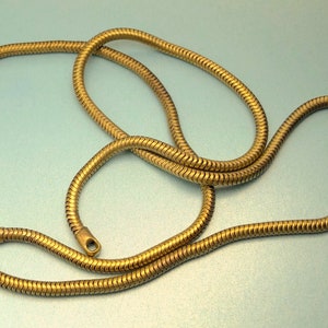 Puede incluir: Un collar de cadena de serpiente de oro. La cadena está hecha de pequeños eslabones entrelazados que crean un aspecto suave y fluido.