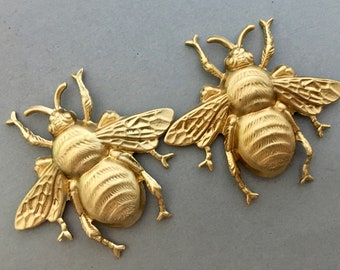 May include: Two gold-colored metal bee figurines with detailed wings and legs. The bees have a textured, striped body.