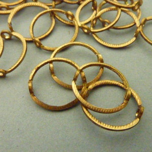 May include: A group of gold-colored metal rings, some are linked together, others are separate. The rings are all the same size and have a textured surface.