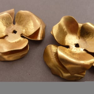 May include: Two gold-colored metal flower-shaped embellishments. Each embellishment has five petals and a small hole in the center.