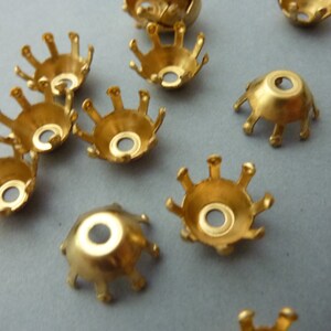 Puede incluir: Un grupo de tapas de cuentas de metal de color dorado con un borde festoneado. Las tapas tienen un pequeño agujero en el centro.
