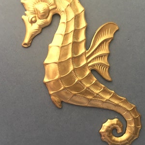 May include: A gold-colored metal seahorse figurine with a detailed design. The seahorse has a curled tail and a fin on its back.